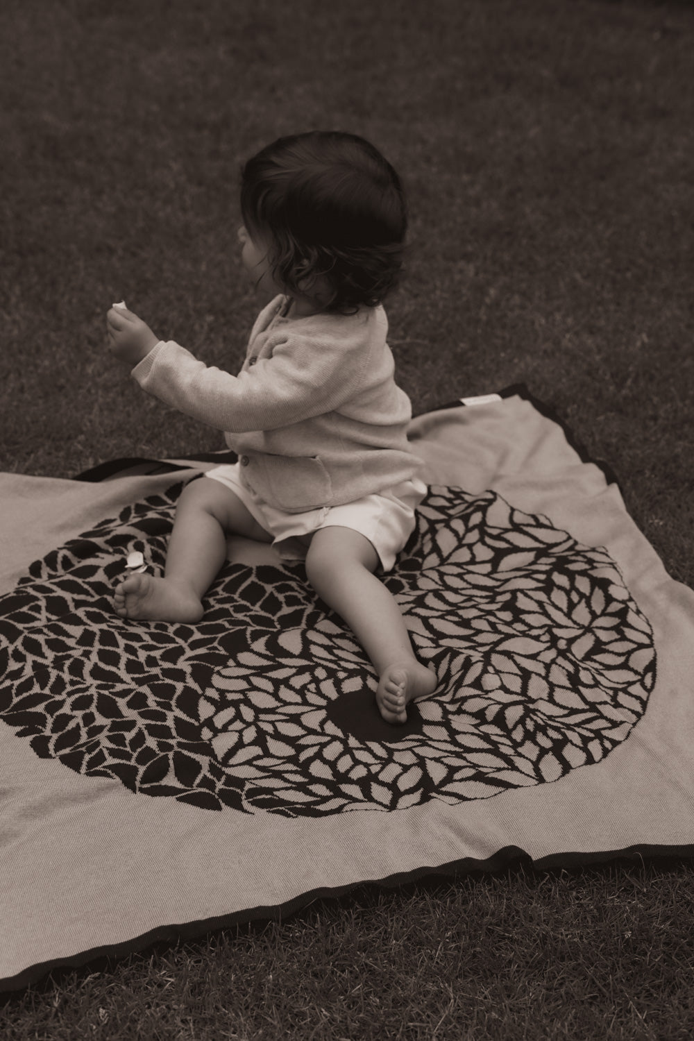 Baby sitzt auf personalisierter Babydecke YIN YANG von LILIMOON im Garten