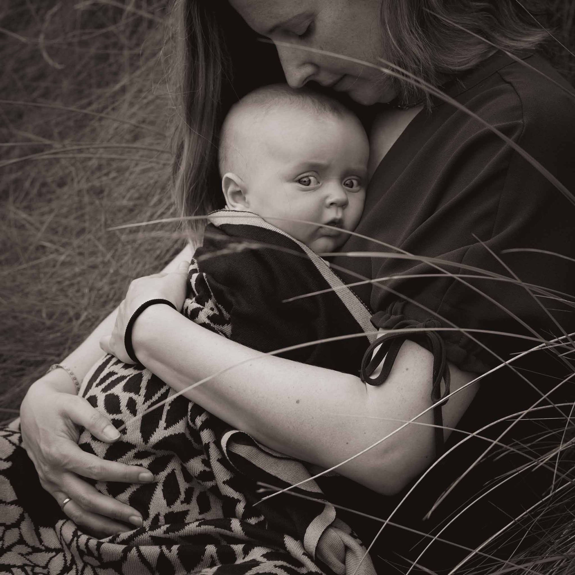 Baby ist eingewickelt in einer Babydecke eingekuschelt im Arm seiner Mama.