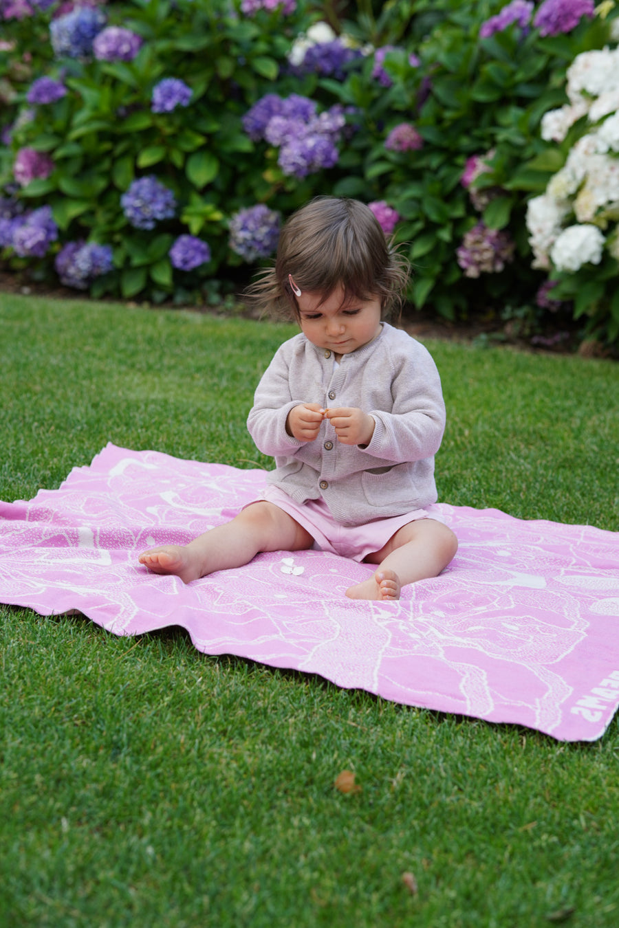 Baby sitzt auf personalisierter Babydecke ROSALIE von LILIMOON im Garten
