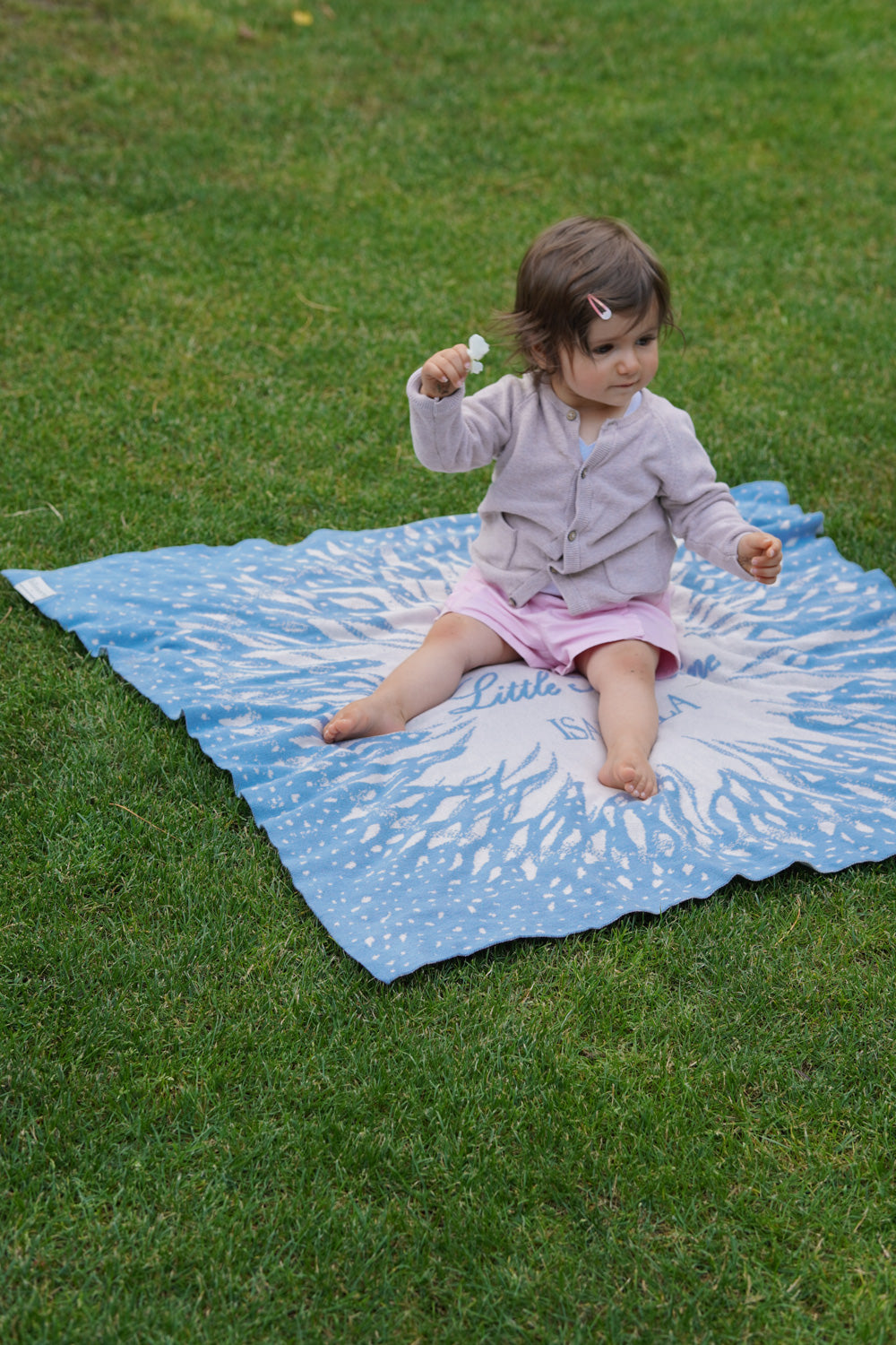 Baby sitzt auf personalisierter Babydecke SUNSHINE von LILIMOON im Garten